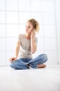 Young woman with mobile phone sitting on the floor dressed casual with curly and long red hair  on white window background Royalty Free Stock Photo