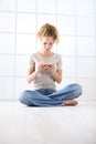 Young woman with mobile phone sitting on the floor dressed casual with curly and long red hair  on white window background Royalty Free Stock Photo