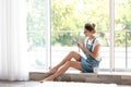 Young woman with mobile phone sitting near window Royalty Free Stock Photo