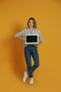 Young woman with modern laptop on yellow background