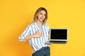 Young woman with modern laptop on yellow