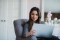 Young woman in modern luxury apartment, sitting comfortable in armchair holding computer on her laps, relaxing, working Royalty Free Stock Photo