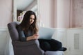 Young woman in modern luxury apartment, sitting comfortable in armchair holding computer on her laps, relaxing, working Royalty Free Stock Photo