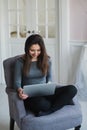 Young woman in modern luxury apartment, sitting comfortable in armchair holding computer on her laps, relaxing, working Royalty Free Stock Photo