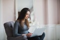 Young woman in modern luxury apartment, sitting comfortable in armchair holding computer on her laps, relaxing, working Royalty Free Stock Photo