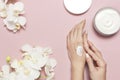 Young woman moisturizes her hand with cosmetic cream lotion opened container with cream body milk White Phalaenopsis