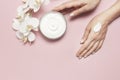 Young woman moisturizes her hand with cosmetic cream lotion opened container with cream body milk White Phalaenopsis Royalty Free Stock Photo