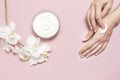 Young woman moisturizes her hand with cosmetic cream lotion opened container with cream body milk White Phalaenopsis orchid