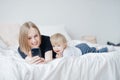 Young woman mom makes selfie photo with baby in bed on cell phone. Concept online chatting Royalty Free Stock Photo