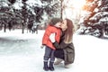 Young woman mother kisses her child, a boy of 3 years. In winter, outdoors in the park, background of snow trees spruce Royalty Free Stock Photo