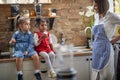 Young woman, mother looking at her daughters enjoying muffins. Two little girls sitting on kitchen countertop, eating muffins Royalty Free Stock Photo