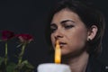 Young woman with a mournful expression on the background of a candle and two red roses, portrait