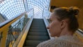 Young woman moving on escalator and looking around in mall Royalty Free Stock Photo