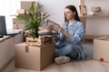 Young woman moving to new place sitting on floor hugging holding frame looking at photo cheerful