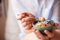 Young woman with muesli bowl. Girl eating breakfast cereals with nuts, pumpkin seeds, oats and yogurt in bowl