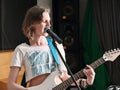 young woman musician playing guitar in studio during rehearsal. rock musician smiling and standing next to a microphone