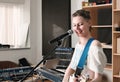 young woman musician playing guitar in studio during rehearsal. rock musician smiling and standing next to a microphone