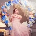 Young woman musician plays the flute while sitting on a swing in flowers. Studio portrait of woman in pink dress Royalty Free Stock Photo