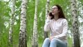 Young woman in nature with a phone. A girl sits on a stump in a birch forest and talks on the phone.