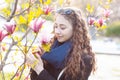 Young woman near blossoming magnolia flowers tree in spring park on sunny day. Beautiful happy girl enjoying smell in a flowering Royalty Free Stock Photo