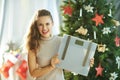 Young woman near Christmas tree showing weight scales