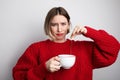 Young woman with negative face showing tea bagging in her cup. Isolated.