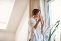 A young woman with night shirt standing by the window in the morning, holding cup of coffee. Royalty Free Stock Photo