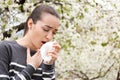 Young woman with nose wiper near blooming tree. Allergy concept