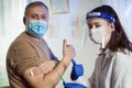 Woman nurse with surgical mask and face shild giving injection to senior man. Covid-19 or coronavirus vaccine Royalty Free Stock Photo