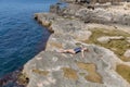 Young woman in one-piece swimsuit resting on rocky seashore Royalty Free Stock Photo