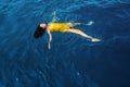 Young woman in a one-piece yellow swimsuit floats on the surface of the water.