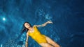 Young woman in a one-piece yellow swimsuit floats on the surface of the water.