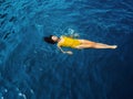 Young woman in a one-piece yellow swimsuit floats on the surface of the water.