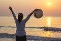 Young woman open arms and holding hat under the sunrise at beach Royalty Free Stock Photo