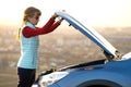 Young woman opening bonnet of broken down car having trouble with her vehicle. Female driver near auto with popped up hood Royalty Free Stock Photo