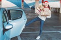 Young woman opening the door in the car with foot in the mall parking with full hands of Christmas gifts