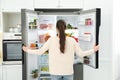 Young woman opening refrigerator in kitchen