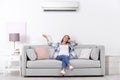 Young woman operating air conditioner while sitting