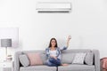 Young woman operating air conditioner while sitting on sofa Royalty Free Stock Photo