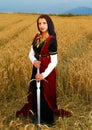 Young woman with ornamental dress and sword in hand standing on a wheat field with sunset. Natural background.. Royalty Free Stock Photo