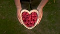 Young woman lowering a heart shaped wooden bowl of fresh red raspberries