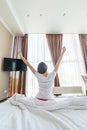 Young woman outstretching her arms sitting on the bed after good night sleep, unwilling to get up and leave her comfortable nest, Royalty Free Stock Photo