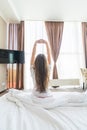 Young woman outstretching her arms sitting on the bed after good night sleep, unwilling to get up and leave her comfortable nest, Royalty Free Stock Photo