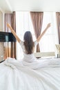 Young woman outstretching her arms sitting on the bed after good night sleep, unwilling to get up and leave her comfortable nest, Royalty Free Stock Photo