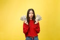 Young woman over yellow wall holding dollars stressed with hand on head, shocked with shame and surprise face, angry and