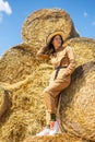 Young woman in overalls and hat at haystack. Female portrait in field in countryside