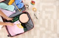 Young woman packing suitcase for summer journey at home