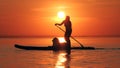 Young woman is paddlesurfing with her dog while the sun is setting