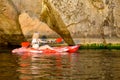 Young Woman Paddling Red Kayak on Beautiful River or Lake under High Rock in the Evening