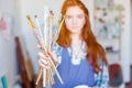 Young woman painter showing dirty paintbrushes in artist workshop